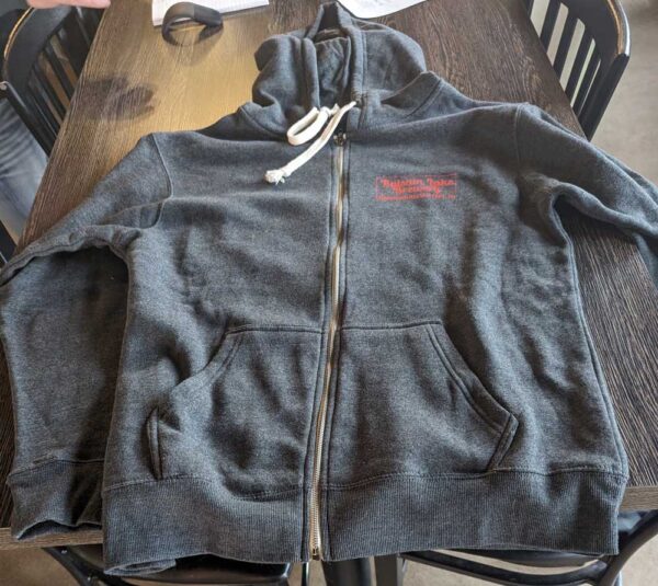 Grey Full Zip Sweatshirt with a logo on the left chest, lying flat on a wooden table.