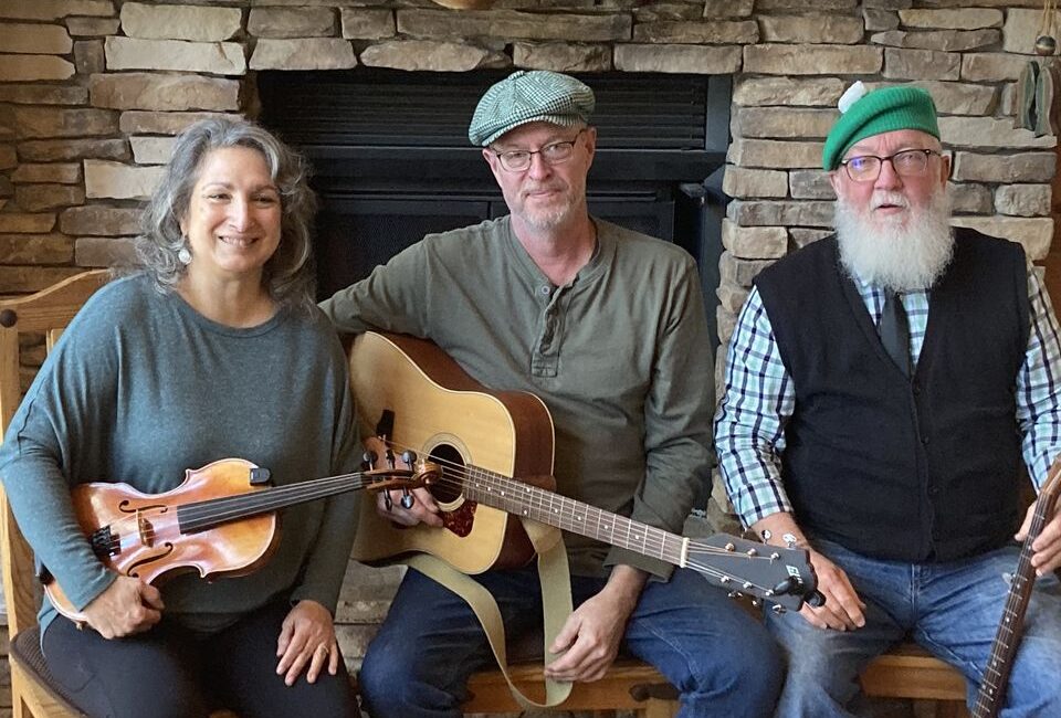 Three people posing with musical instruments in front of a stone fireplace.