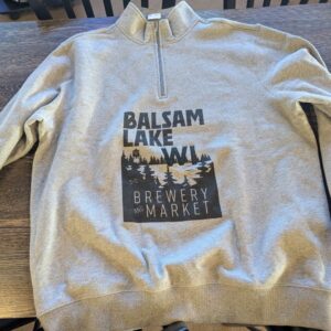 Quarter Zip Sweatshirt Grey displaying "Balsam Lake WI Brewery and Market" with a woodland graphic, situated on a wooden table.