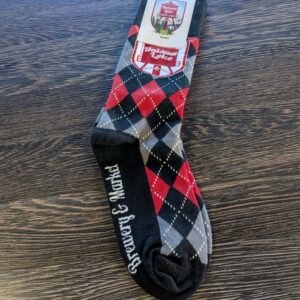 A pair of Brewery Socks in a black, red, and gray argyle pattern with "Scotland Forever" written on them, placed on a wooden surface.