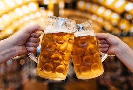 Two hands clinking large glass mugs filled with beer in a celebratory toast, with a warmly lit background.