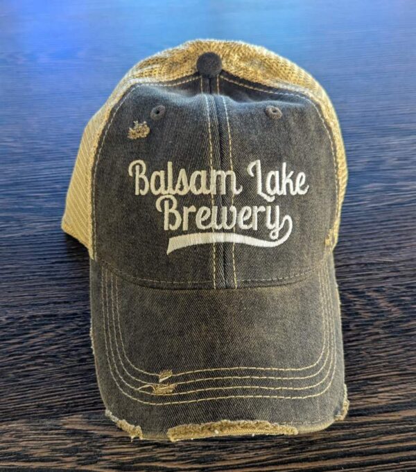 A "Distressed Baseball Cap Black" featuring "Balsam Lake Brewery" embroidered on the front, laid out on a wooden surface.